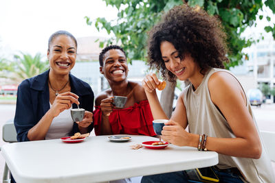 Smiling friends using smart phone while sitting at restaurant