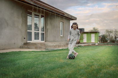 Cute little girl playing football with soccer ball on green lawn in backyard of house. child kicking