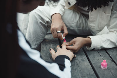 Midsection of boy painting fingernails of male friend with pink polish at table