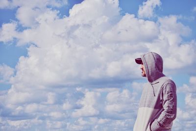 Side view of mid adult man wearing hooded shirt while against cloudy sky