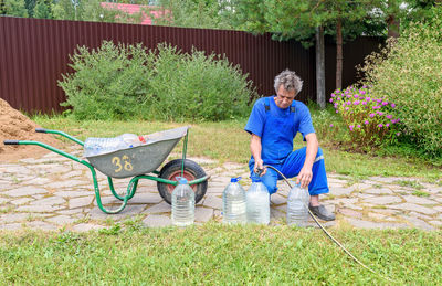 Man in a blue jumpsuit pours drinking water from a hose into large bottles. 