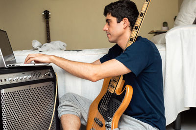 Casual man using a laptop to learn to play electric bass at home.