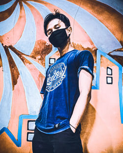 Full length of young man standing against graffiti wall