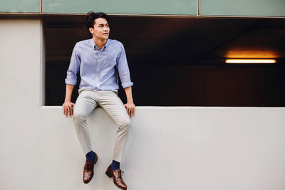 Young man looking away while standing against wall