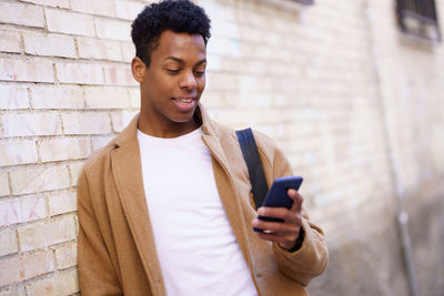 Young man using mobile phone against wall