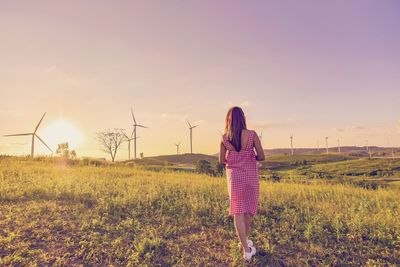 Rear view of woman walking on agricultural field against sky during sunset