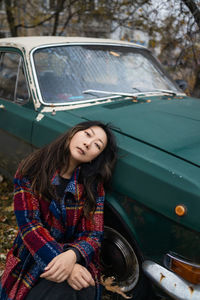 Portrait of young woman standing against car