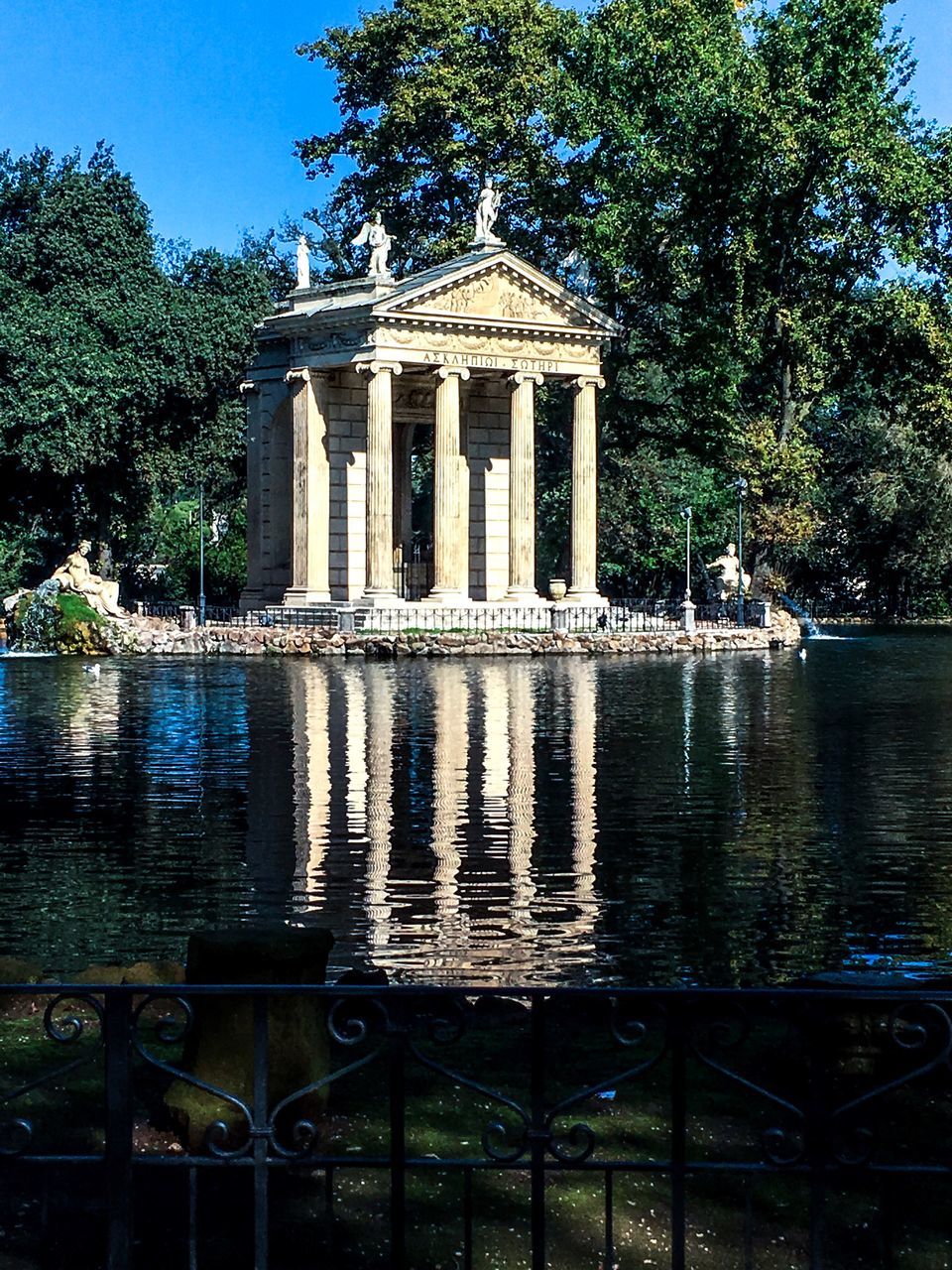 tree, architecture, built structure, water, reflection, building exterior, travel destinations, architectural column, famous place, tourism, outdoors, surface level, monument, in front of, history, the past, facade, garden, national landmark, waterfront