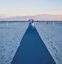 Rear view of boy running on blue carpet at jones beach