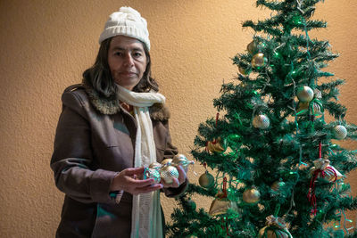 Old woman puts spheres and decorations on the christmas tree, new year