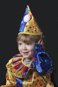 Smiling boy in clown costume sitting against black background