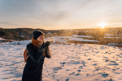 A woman blows snow from her palms on a sunny winter evening