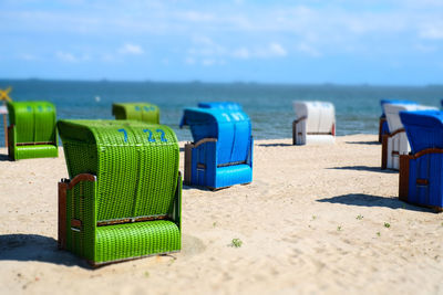 Hooded chairs on sand at beach against sky