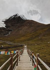 Wooden footbridge leading towards mountains against sky