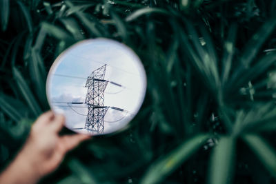 Close-up of hand holding mirror with reflection of electricity power lines