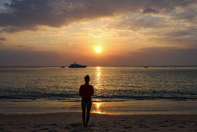 Rear view of man standing on beach during sunset