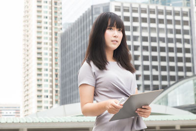 Young businesswoman standing against buildings in city