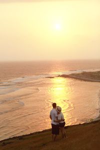 Rear view of couple looking at sea against sunrise sky