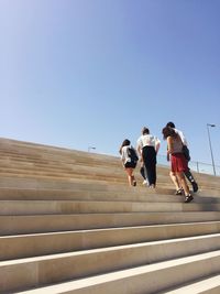 Low angle view of friends walking on staircase against clear blue sky