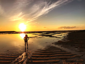 Silhouette person standing on beach against sky during sunset