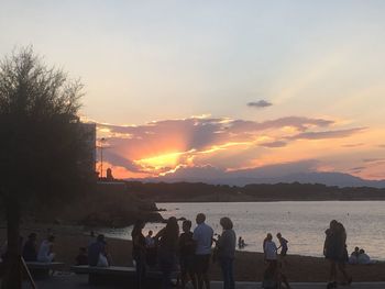 Silhouette people by sea against sky during sunset