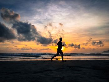 Silhouette man running on beach against sky during sunset