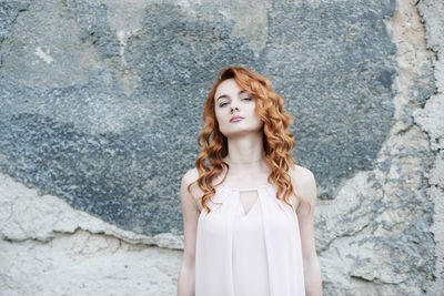 Portrait of young woman standing against wall