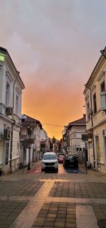 Cars on street by buildings against sky during sunset