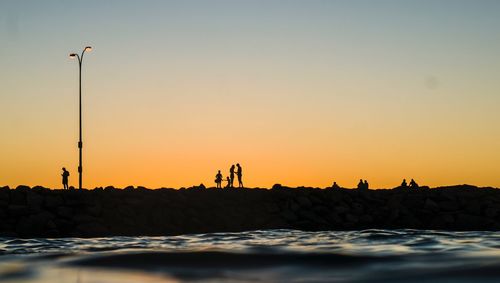 Silhouette people at beach against clear sky during sunset