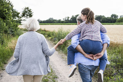 Grandmother holding hand of granddaughter while playing with piggybacking on grandfather