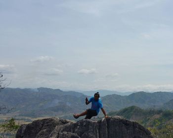 Man on rock formation against sky