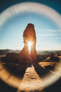 Sun shining through rock formation against sky