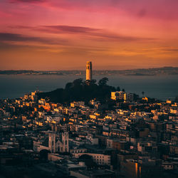 Aerial view of cityscape by sea against sky at sunset