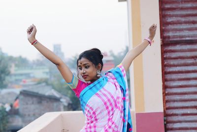 Woman wearing sari with arms raised standing in balcony