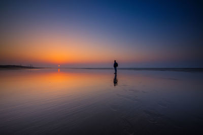 Silhouette man standing on beach against sky during sunset