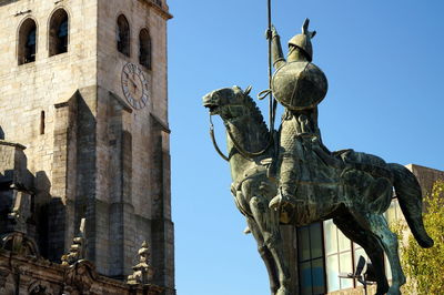Low angle view of equestrian statue against old building porto cathedral against clear sky