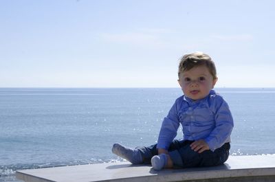 Baby boy sitting on beach against sky