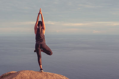 Full length of woman climbing on sea shore against sky