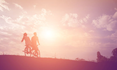 Silhouette people riding bicycle against sky during sunset