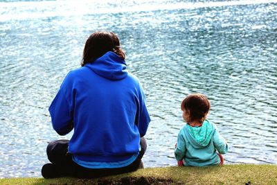 Rear view of woman and daughter sitting on grass by sea