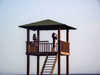 Women standing in lifeguard hut against sky