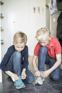 Young boys tying shoe laces on floor