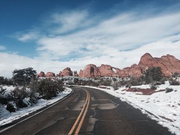 Empty road along snow covered mountains against sky