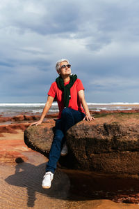 Portrait of man sitting on rock by sea against sky