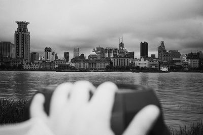 Reflection of man photographing water on city buildings against sky
