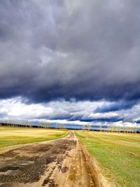 Empty road amidst field against sky