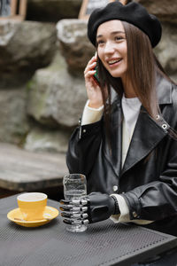 Smiling young woman talking on phone while sitting at cafe