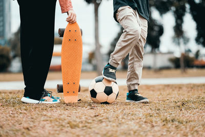 Low section of friends with skateboard and soccer ball on field