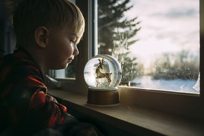 Side view of boy looking at decor on window sill at home