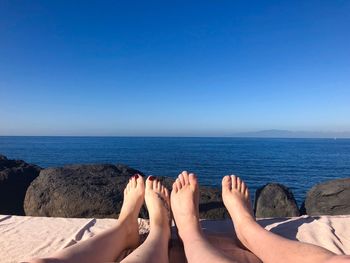 Low section of friends at beach against blue sky